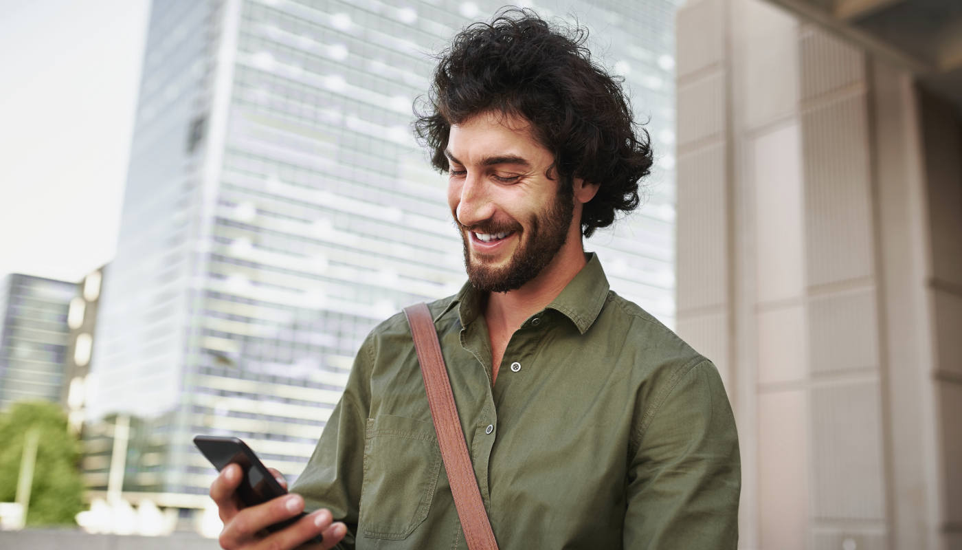 Ein lächelnder junger Mann verwendet sein Smartphone unterwegs. 
