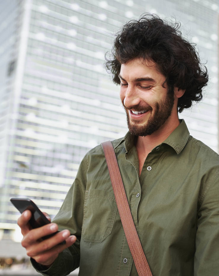 Ein lächelnder junger Mann steht auf der Straße und nutzt sein Smartphone.