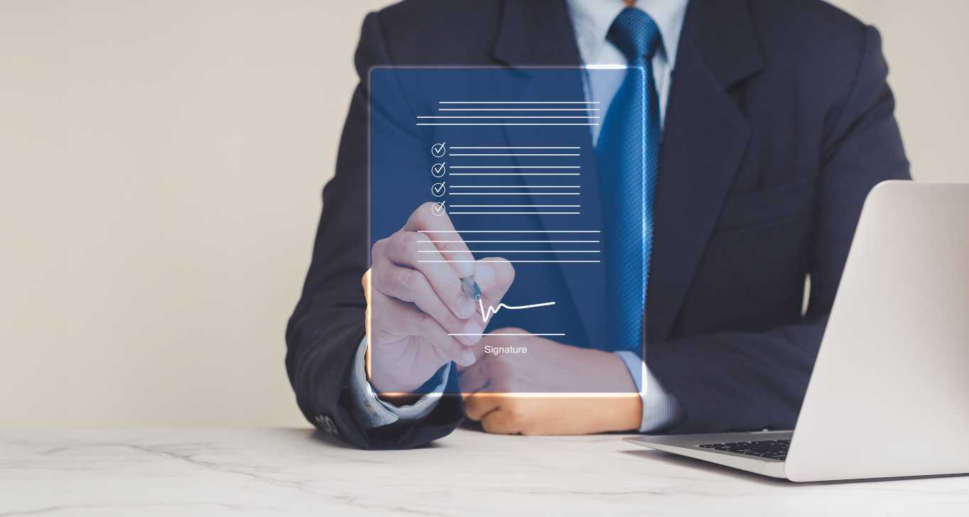 Montage: A businessman sits at a table with a laptop in front of him; a symbol representing a document floats in front of him, which he signs with a pen.