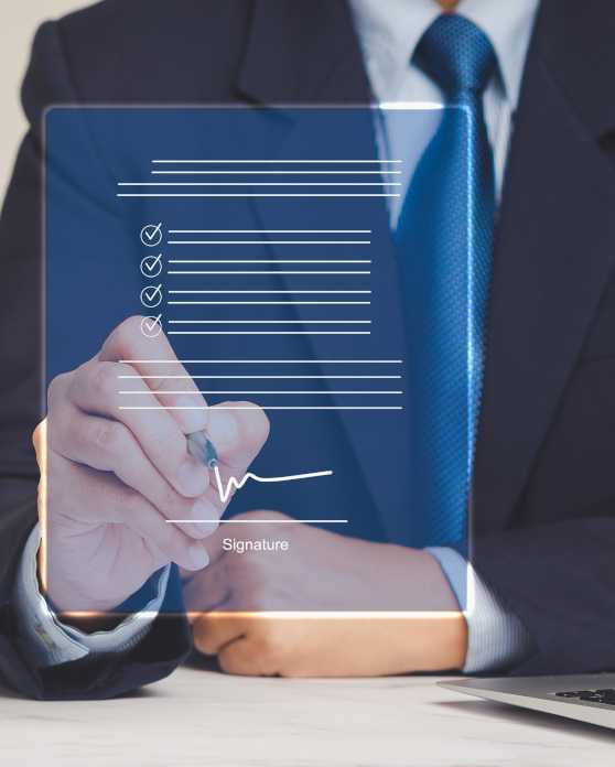 Montage: A businessman sits at a table with a laptop in front of him; a symbol representing a document floats in front of him, which he signs with a pen.