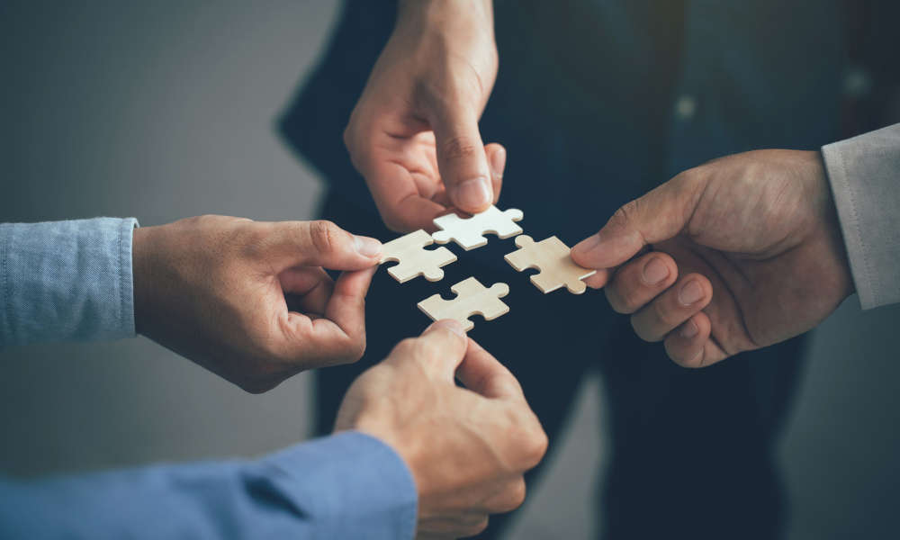 Mood picture: Four people symbolize teamwork by putting four matching puzzle pieces together to form a whole.