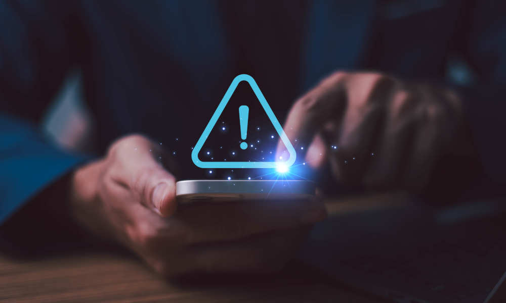 Montage: Person holding a smartphone in a dark environment. Above the display, a glowing blue warning triangle icon with an exclamation mark.