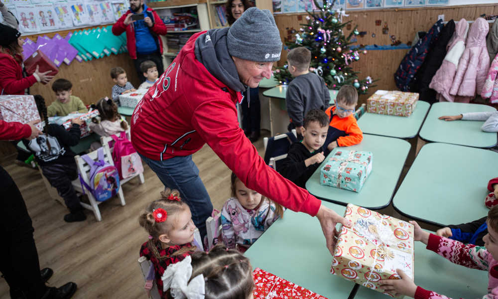 Sven Glöckner handing a Christmas gift package to a young girl, with other children sitting happily nearby in front of their presents.