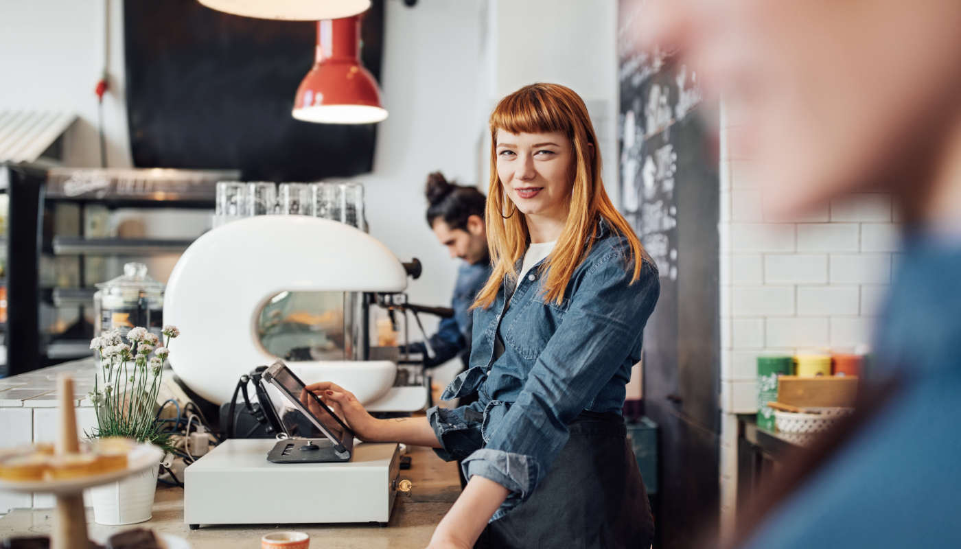 Friendly young woman operating a cash register in a café.