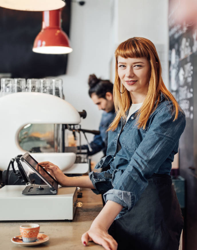 Friendly young woman operating a cash register in a café.