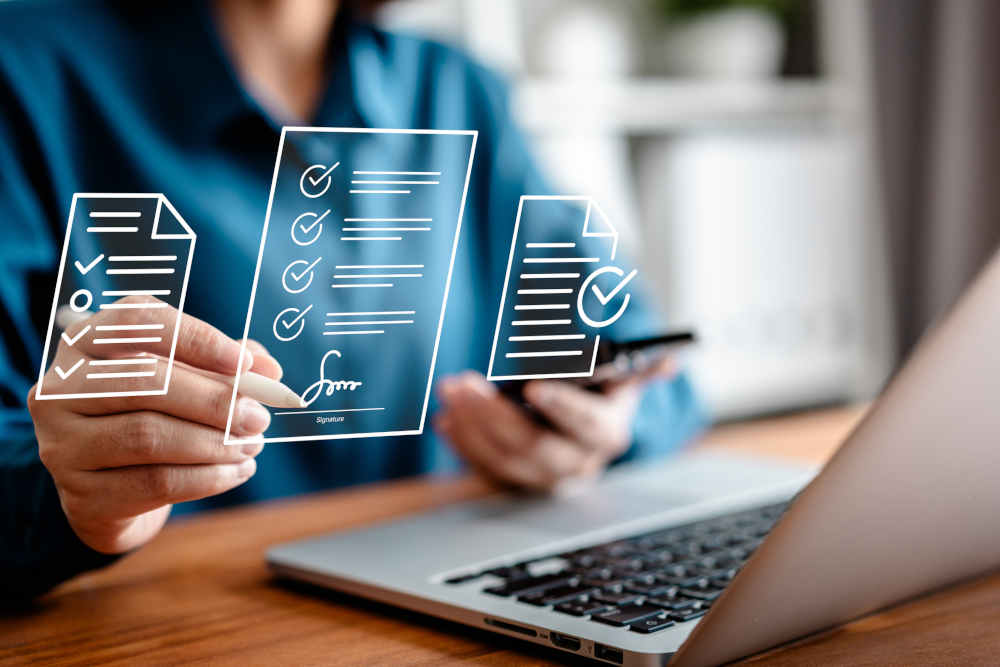 Montage: Person sitting at a laptop, holding a smartphone in the left hand and signing digital documents with a stylus in the right hand; The documents are shown as floating icons in the foreground.