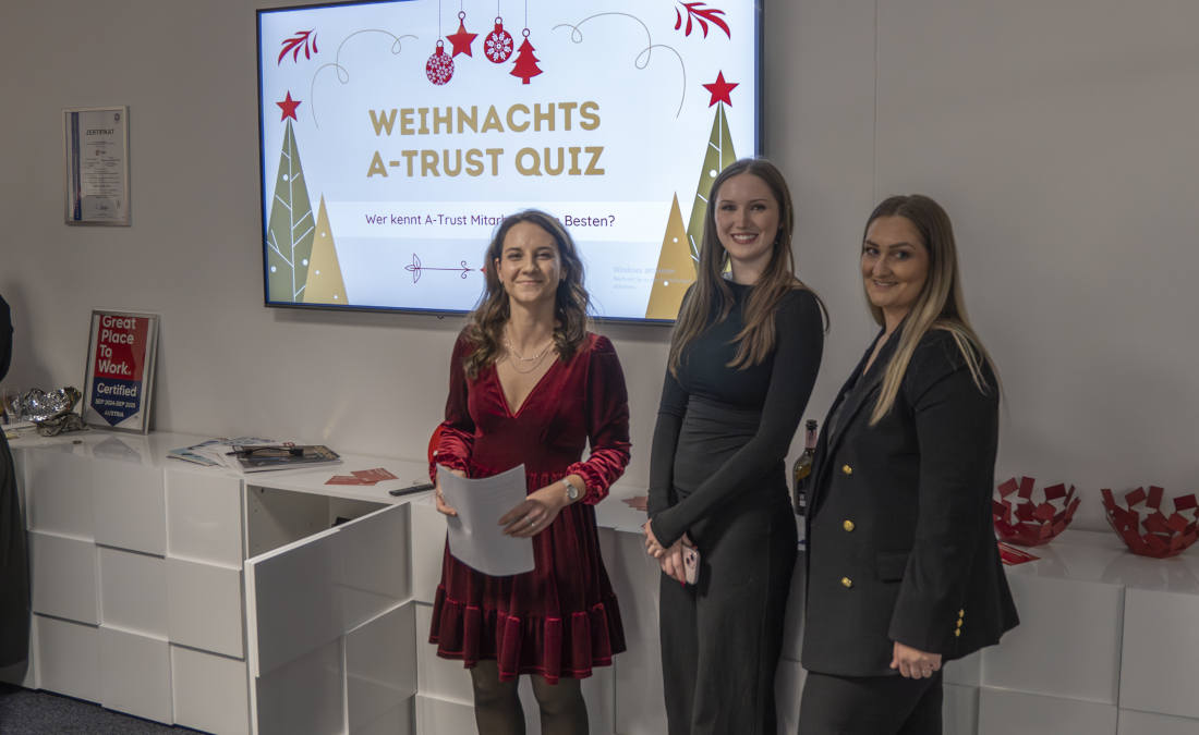 Drei Mitarbeiterinnen präsentieren ein A-Trust Weihnachtsquiz auf einem Bildschirm im Unternehmen