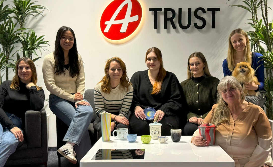 A-Trust Mitarbeiterinnen sitzen auf einer Couch im Foyer; vor ihnen stehen bemalte Keramikkunstwerke